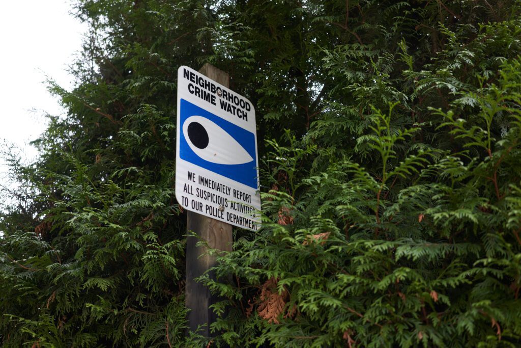 A neighborhood crime watch sign on a poll surrounded by trees.
