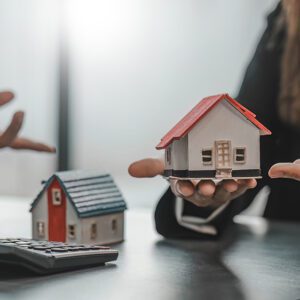 hand holding a house with another set of hands in distance and calculator